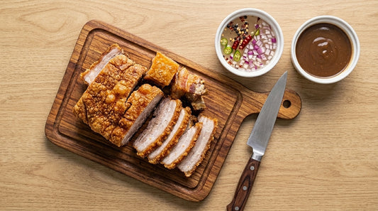  A cutting board displaying pork bagnet and pork crackling, accompanied by a small bowl of dipping sauce.
