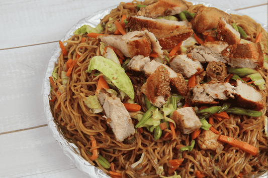  A serving of lechon belly and pancit in a metal dish, showcasing traditional Filipino comfort food in the UK.
