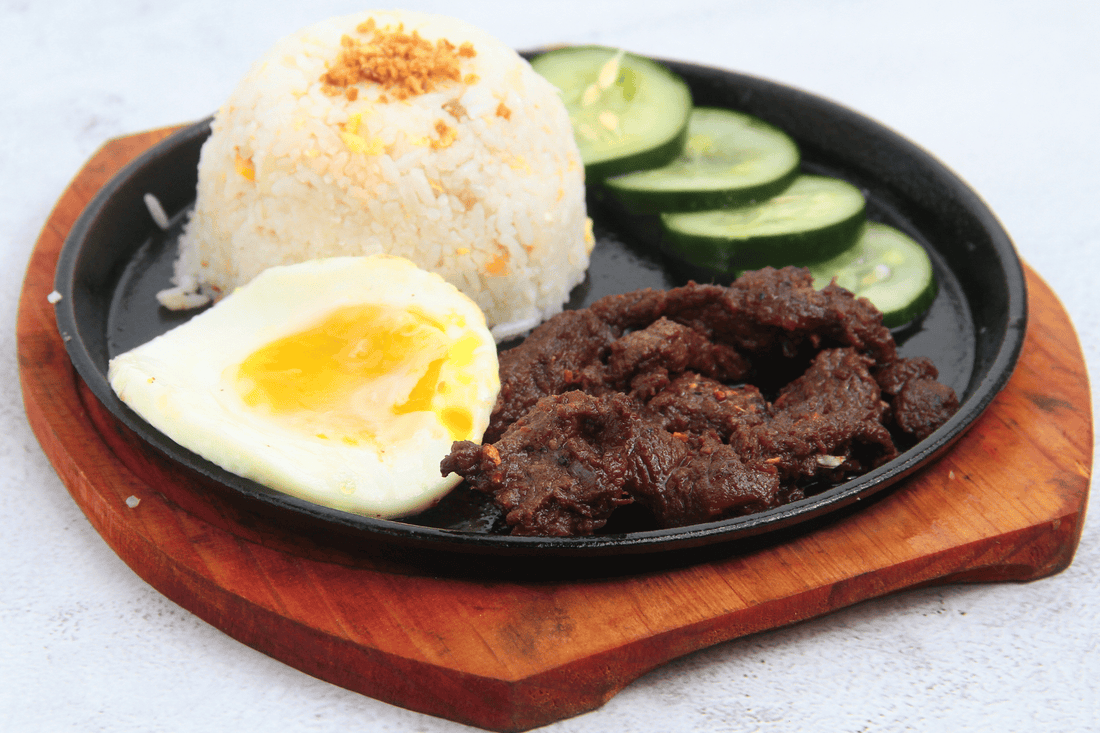 A plate of tapsilog featuring garlic rice, marinated beef, and a sunny-side-up egg, typical of a Filipino breakfast.