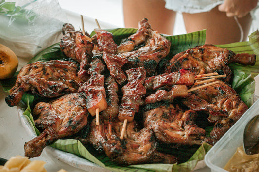  A plate of skewered meat is displayed, with a woman standing next to it, highlighting Filipino barbecue and chicken inasal.