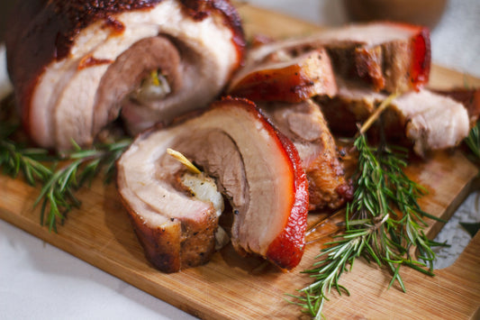 Sliced lechon belly on a cutting board, garnished with fresh rosemary, showcasing a traditional Filipino celebration dish.