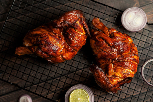 Two marinated chicken breasts cooling on a rack, accompanied by fresh onions and lime slices.