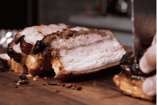  Close-up of a person cutting pork bagnet, highlighting its crispy skin and tender meat on a rustic cutting board.
